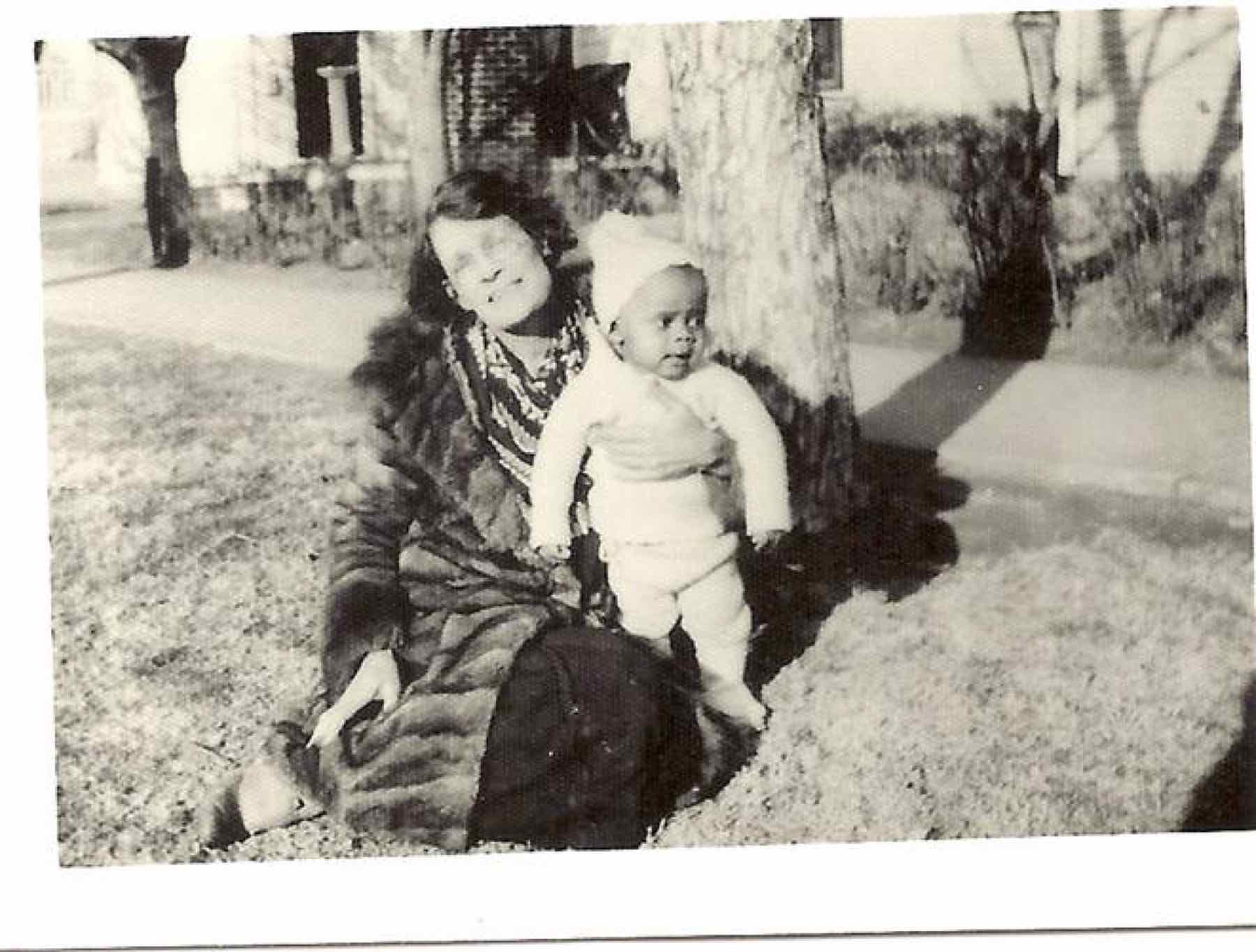 A woman seated on a lawn in a fur coat with a toddler in a knit cap and suit. From the Jackson family collection; the sitters are not identified in the collection records.